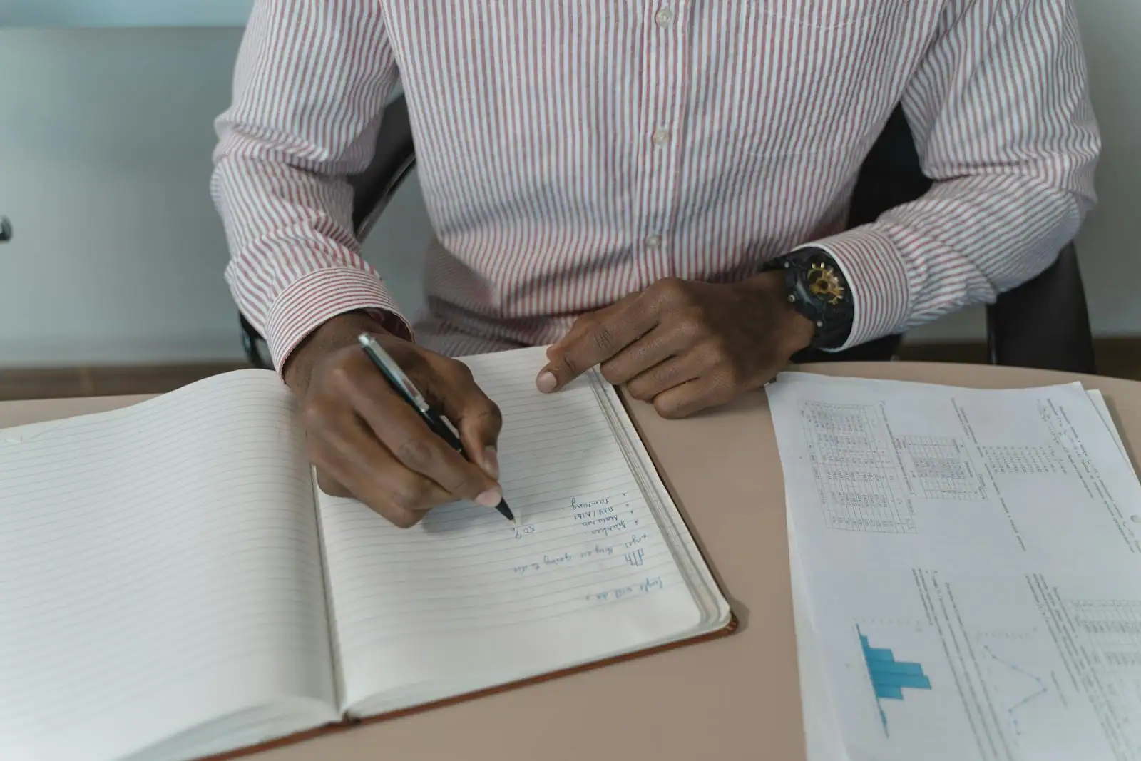 Porteur de projet rédigeant son business plan dans un carnet, à côté de graphiques et d'un ordinateur