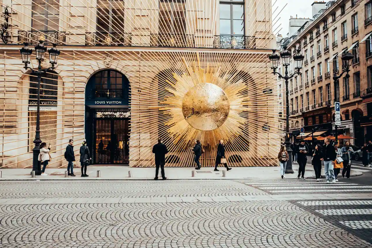 Façade de la boutique Louis Vuitton à Paris, avec son décor doré en rayons de soleil et des passants dans la rue