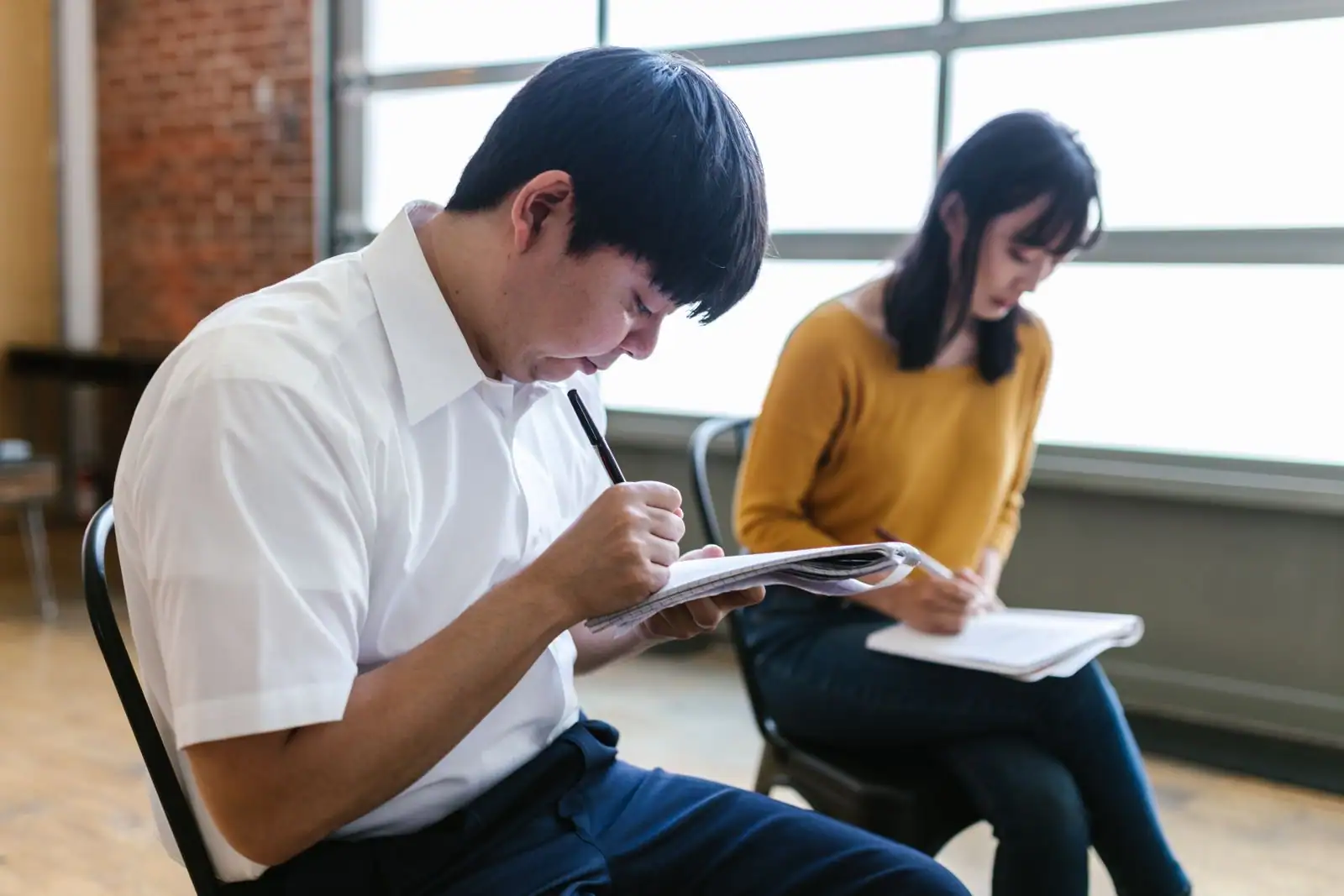 Deux adultes assis prennent des notes sur des cahiers pendant une session de formation