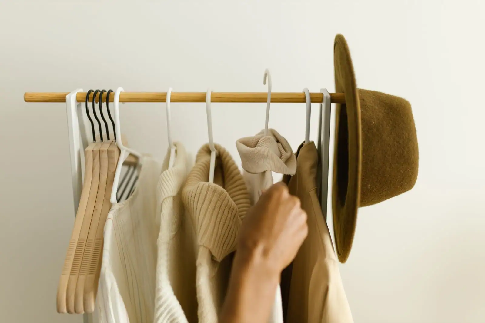 Une main parcourt des vêtements suspendus sur un portant, comme lors d'une bourse aux vêtements