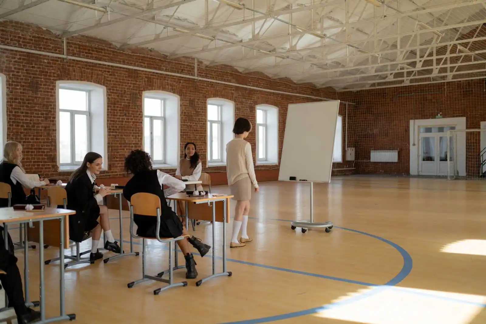 Élèves adolescents assis à des pupitres dans un grand hall scolaire, devant un tableau blanc