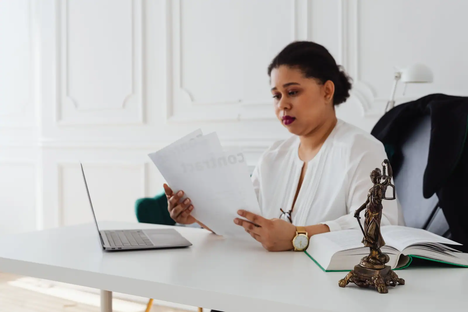 Professionnelle du droit examinant un contrat à son bureau, près d'une statuette de la Justice.