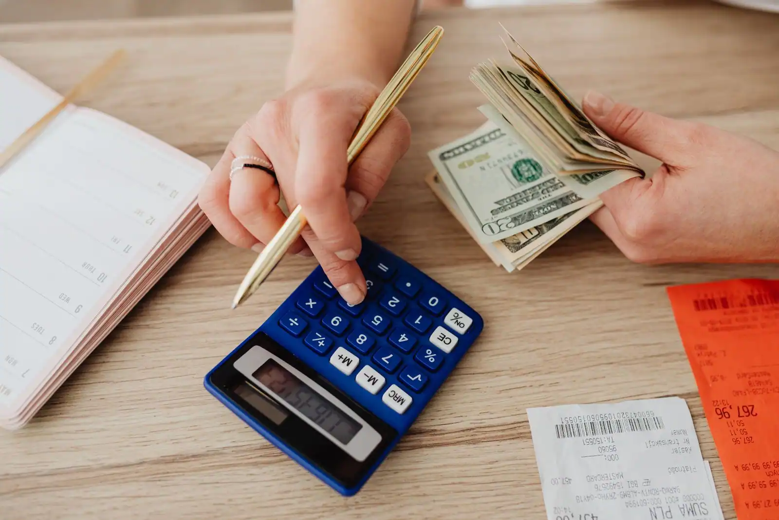 Mains comptant des billets avec une calculatrice et un agenda, scène de calcul de budget sur un bureau.