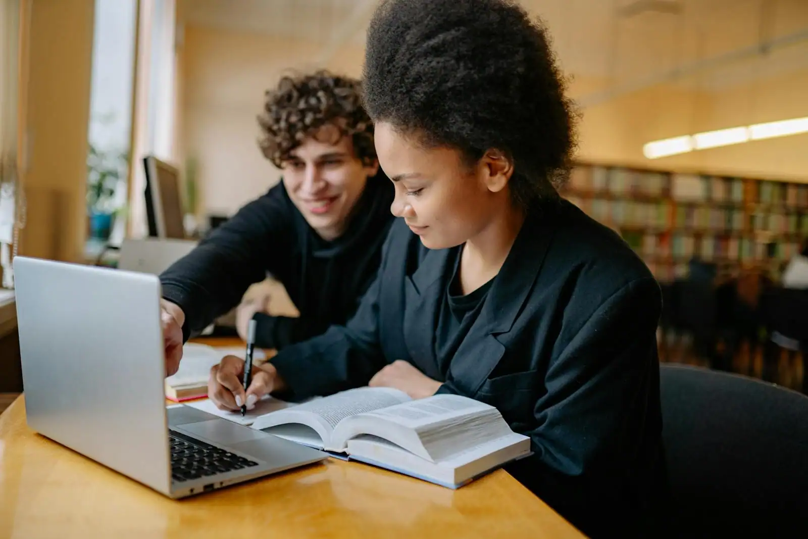 Deux étudiants travaillant ensemble avec un ordinateur portable et un livre ouvert dans une bibliothèque