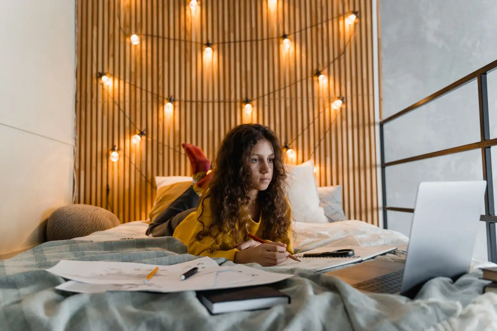 Adolescente qui révise allongée sur son lit avec des cahiers et un ordinateur portable
