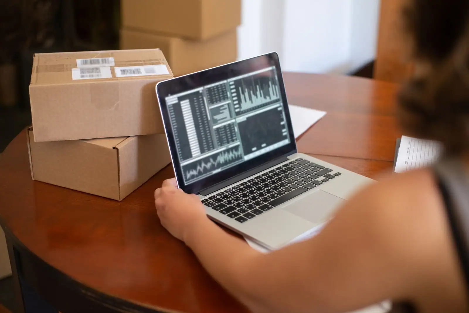 Entrepreneur gérant son activité en ligne, ordinateur portable et colis à expédier sur son bureau.