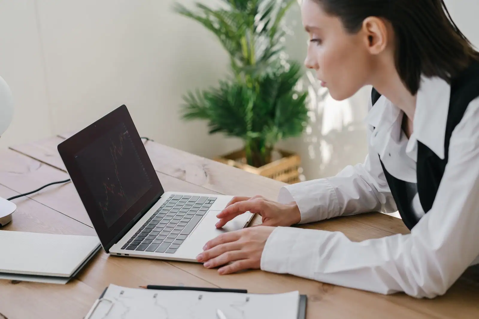 Femme en chemise blanche travaillant sur un ordinateur portable, un graphique affiché à l'écran.