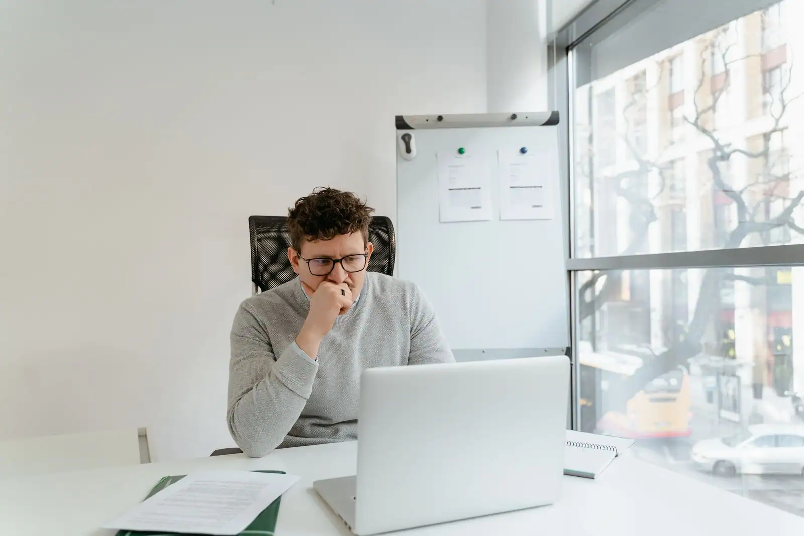 Un professionnel installé seul à son bureau travaille sur un ordinateur portable, concentré, près d'une grande fenêtre.
