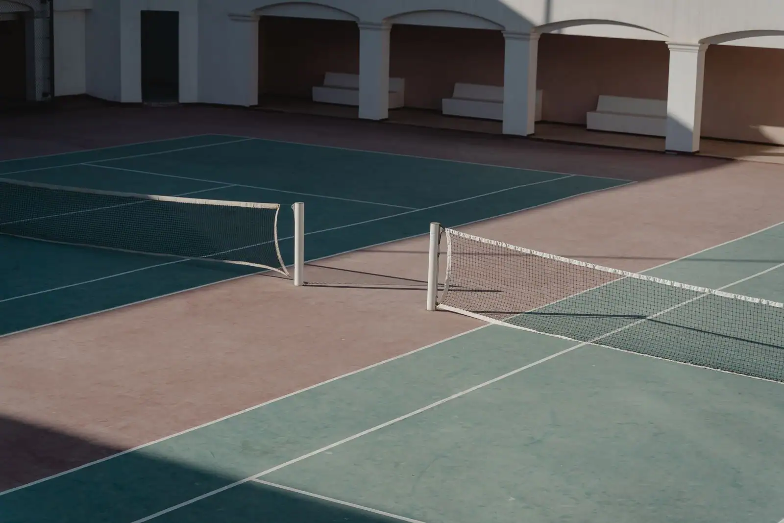 Deux courts de tennis vides avec leurs filets, dans une installation couverte de club.