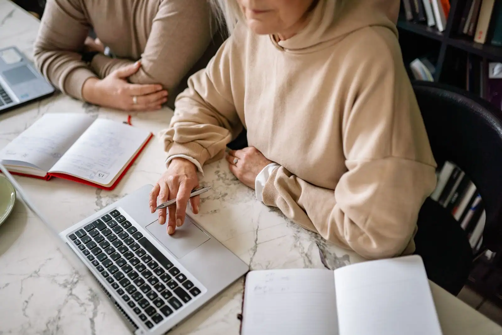 Femme d'âge mûr utilisant un ordinateur portable, des cahiers de notes ouverts sur le bureau