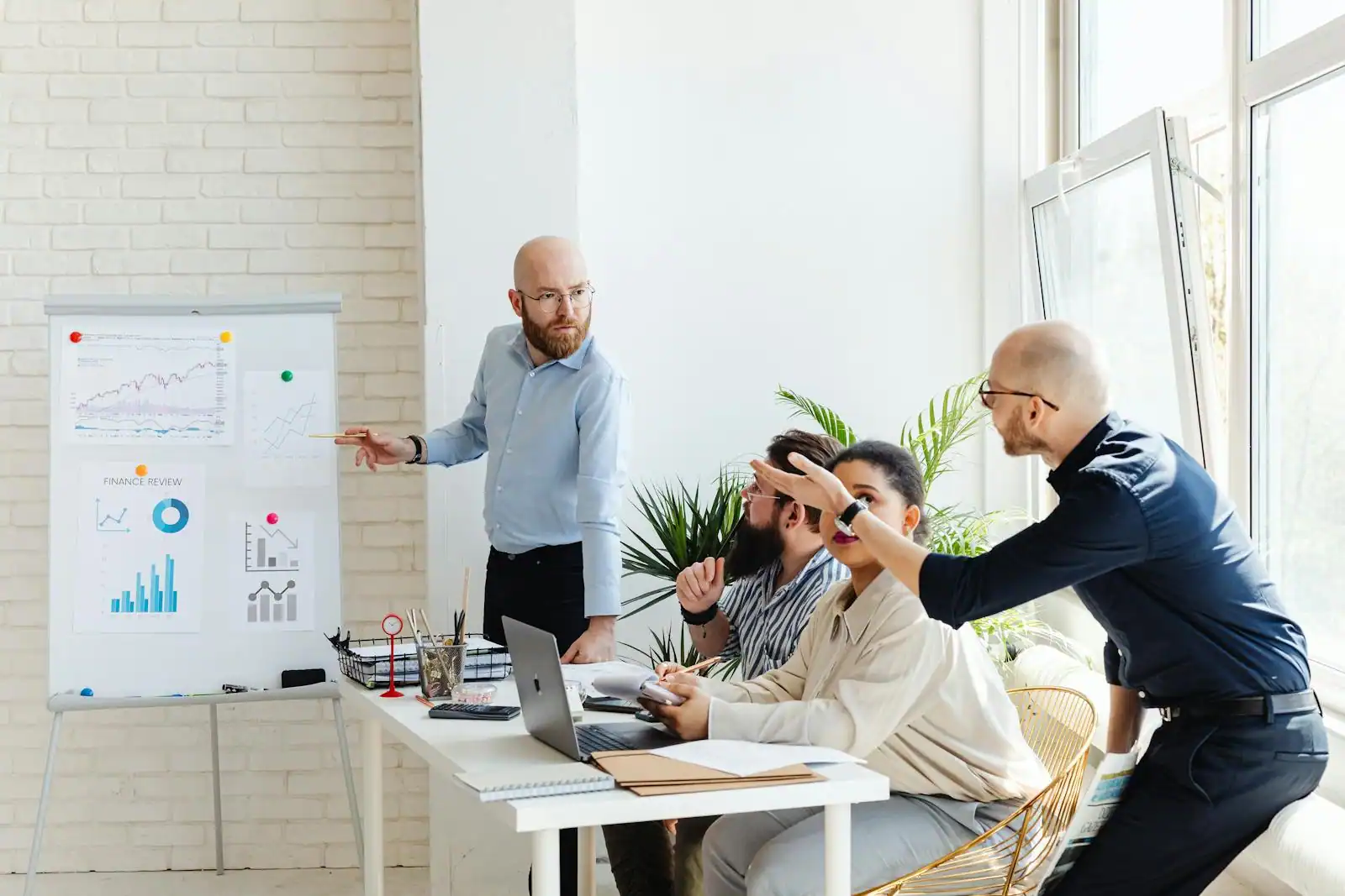 Équipe de quatre personnes en réunion de travail dans un bureau, autour d'un tableau de présentation et d'un ordinateur portable