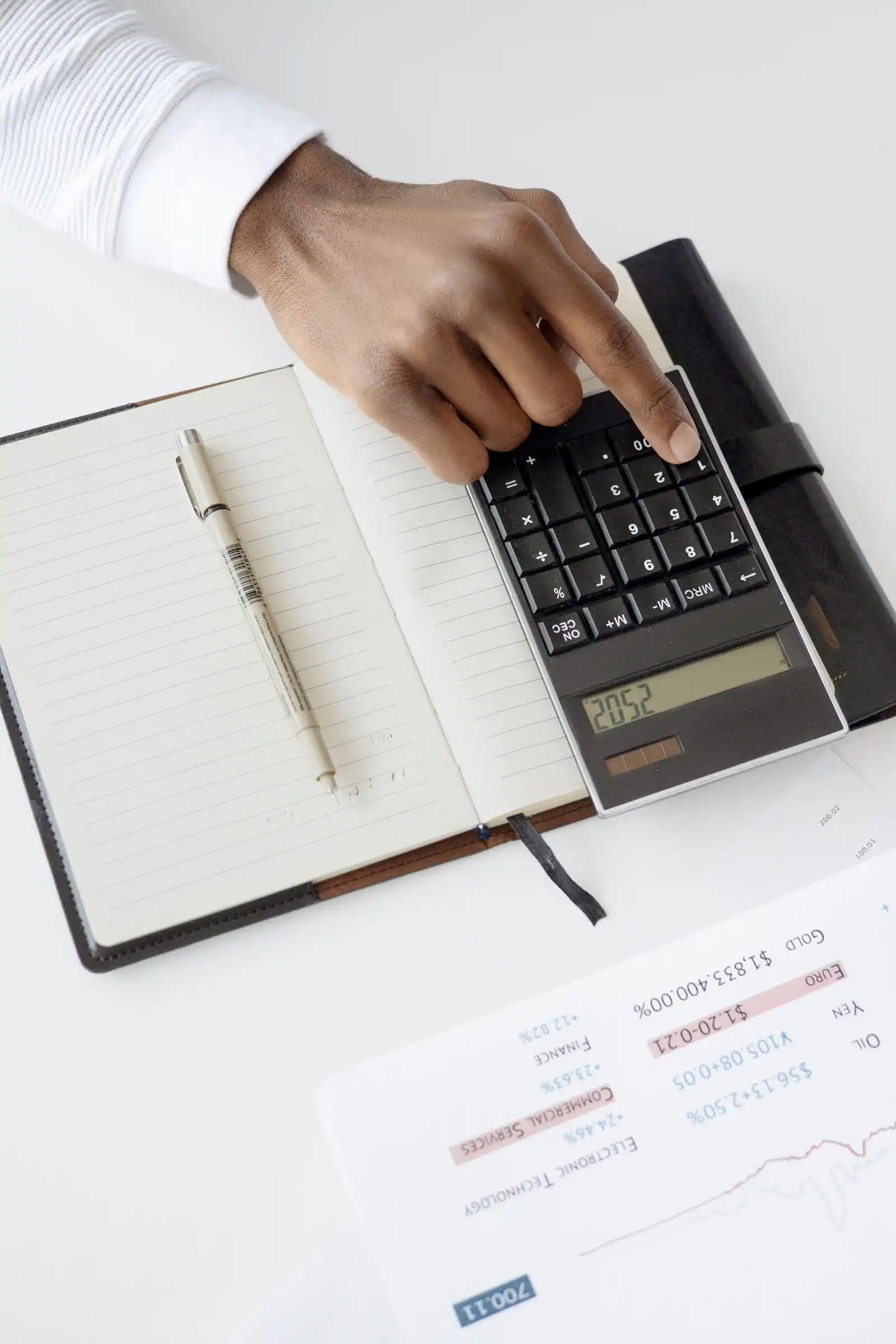 Main utilisant une calculatrice posée sur un carnet, à côté d'une feuille de données financières
