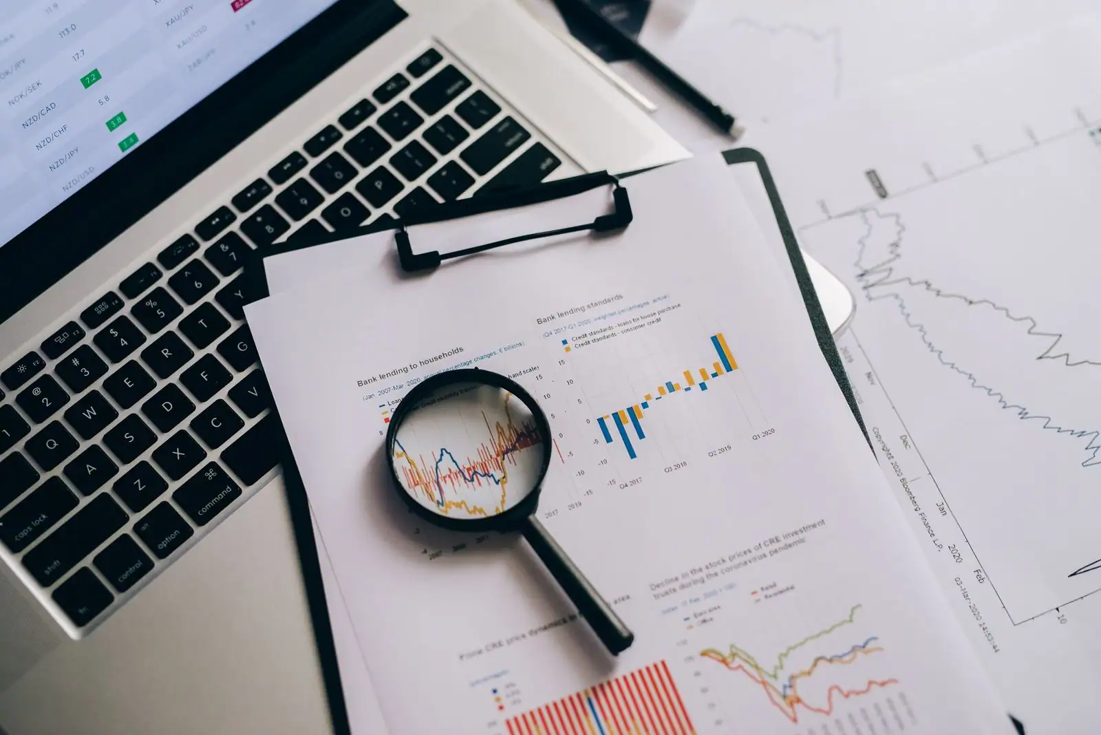 Des graphiques financiers imprimés examinés à la loupe, à côté d'un ordinateur portable, sur un bureau.