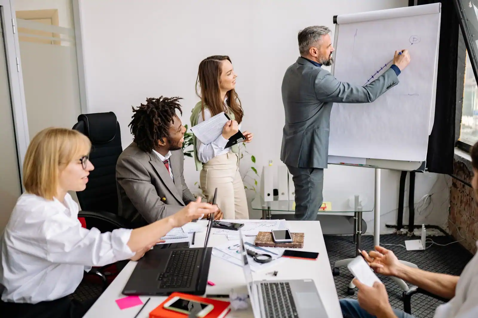 Un responsable présente au paperboard devant son équipe réunie dans un bureau lumineux.