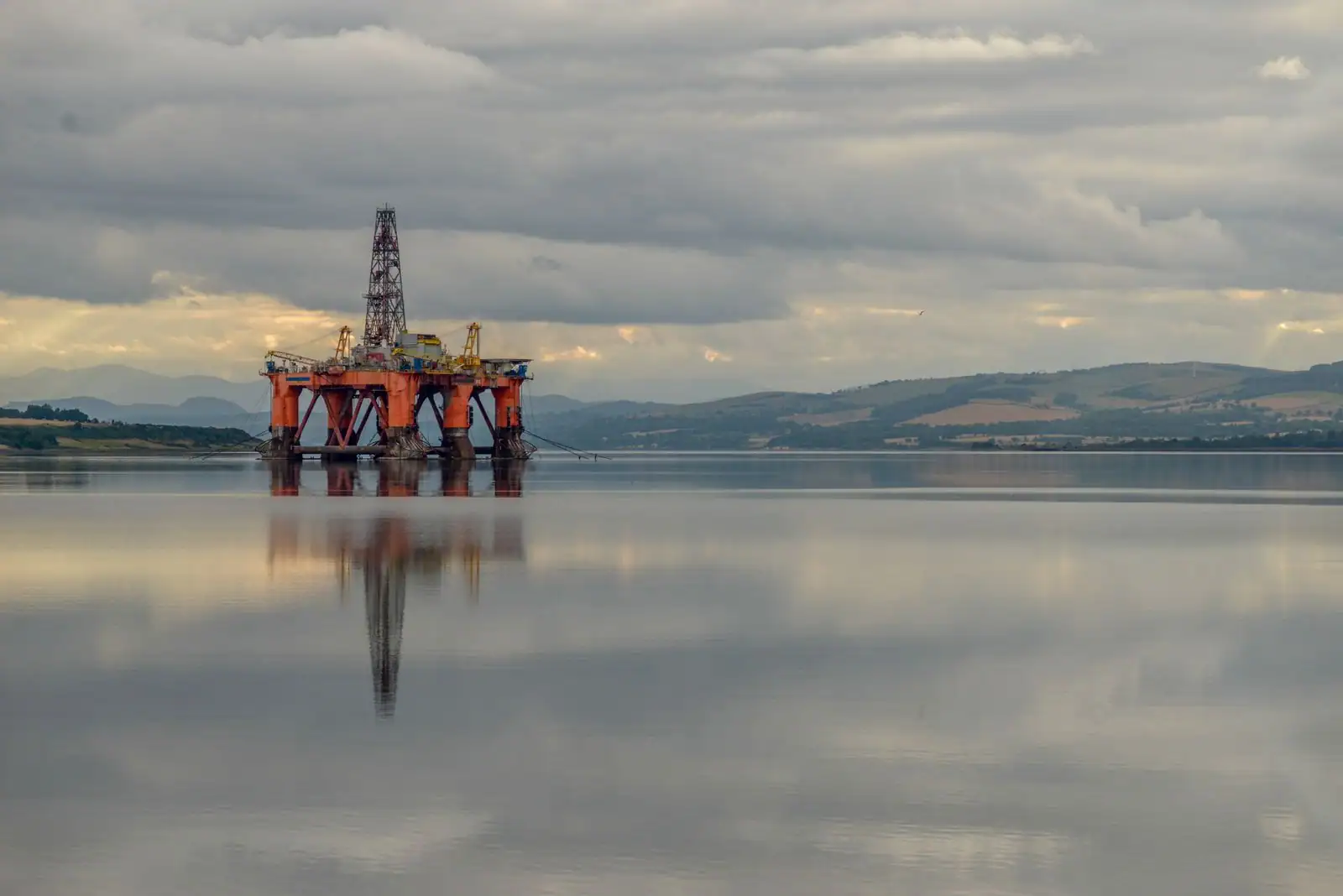 Une plateforme pétrolière offshore aux structures métalliques oranges se dresse sur une eau calme.