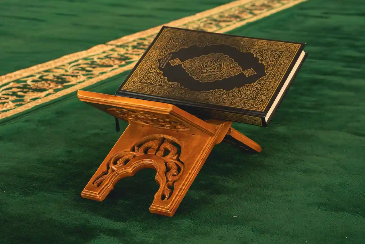 Coran à la couverture calligraphiée, posé fermé sur un lutrin en bois sculpté