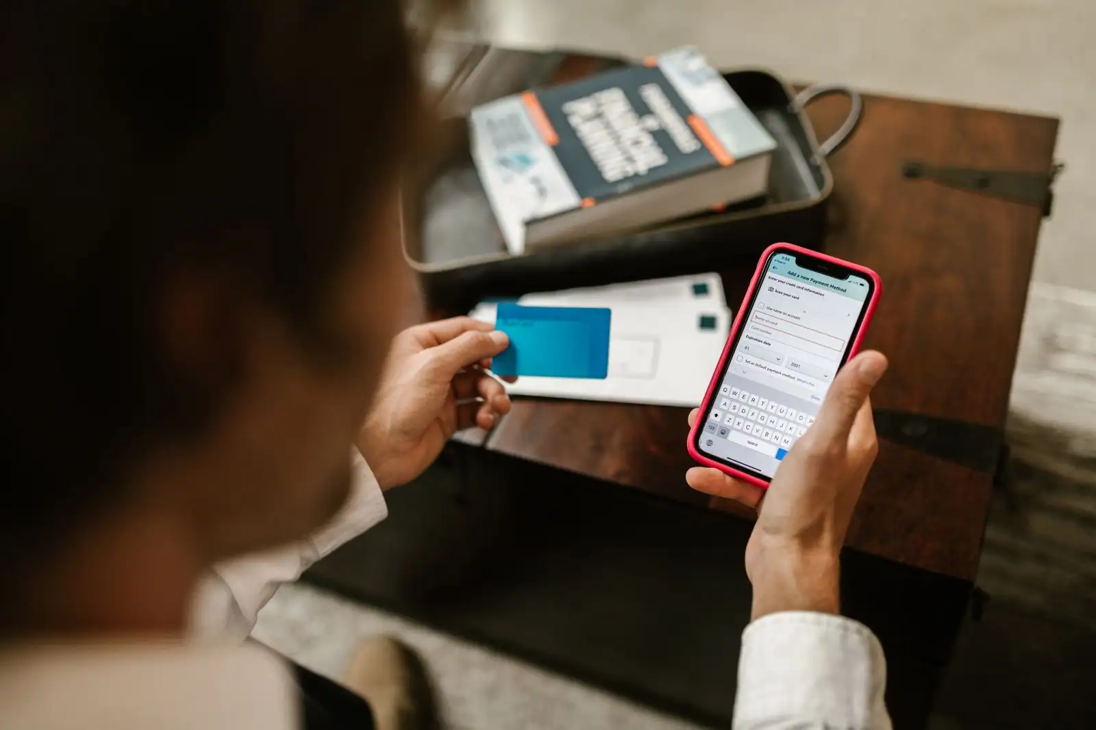 Personne effectuant un paiement en ligne sur l'application bancaire de son smartphone, carte à la main