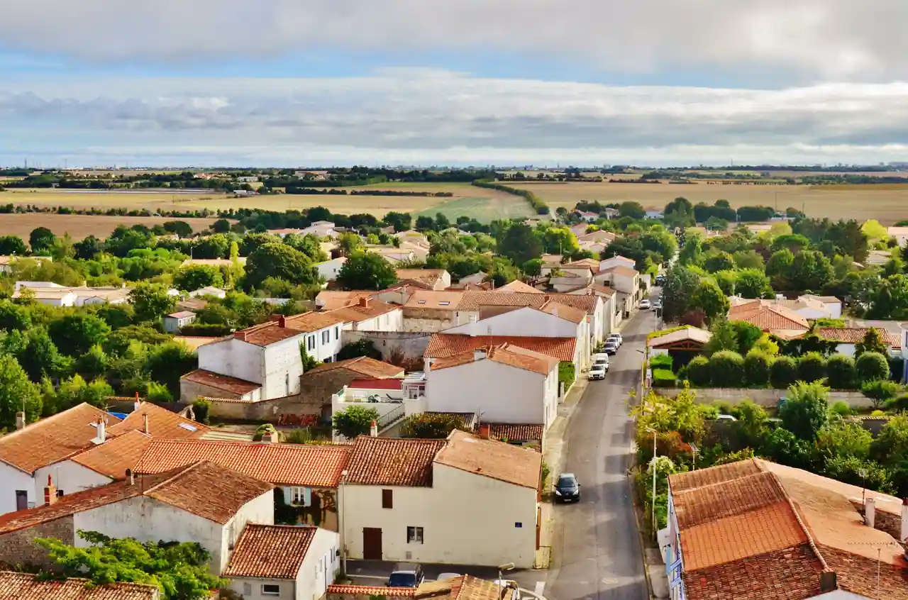 Vue aérienne d'un village aux toits de tuiles et de sa rue principale, entouré de champs cultivés.