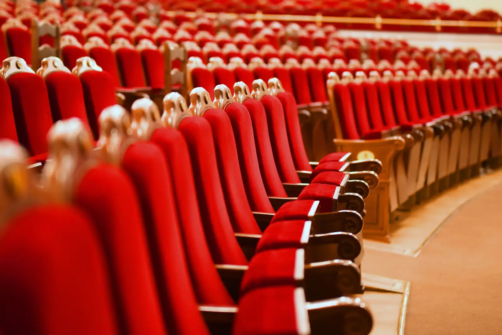 Rangées de fauteuils de théâtre en velours rouge, vides, avec leurs accoudoirs de bois sculpté.
