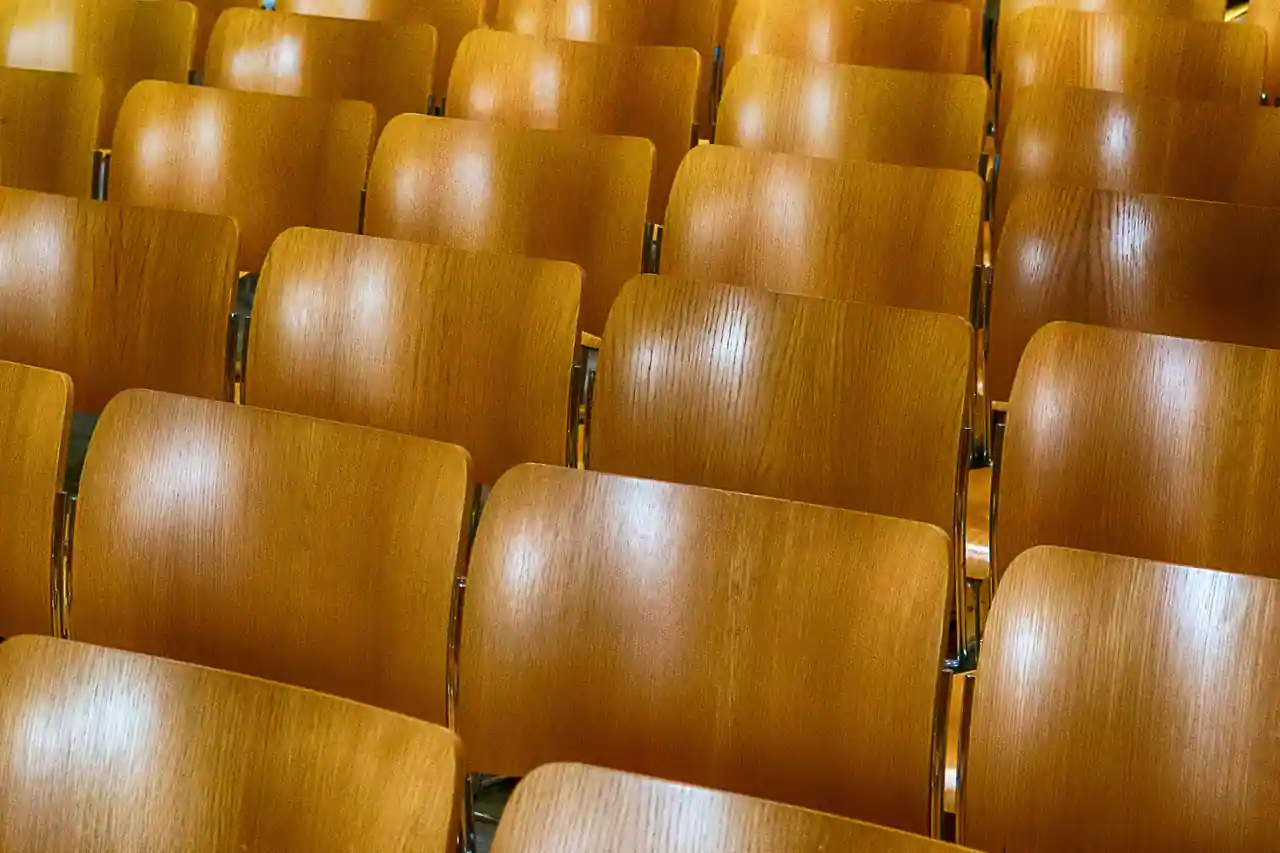 Rangées de sièges en bois clair alignés dans une salle de réunion vide, vues de près.