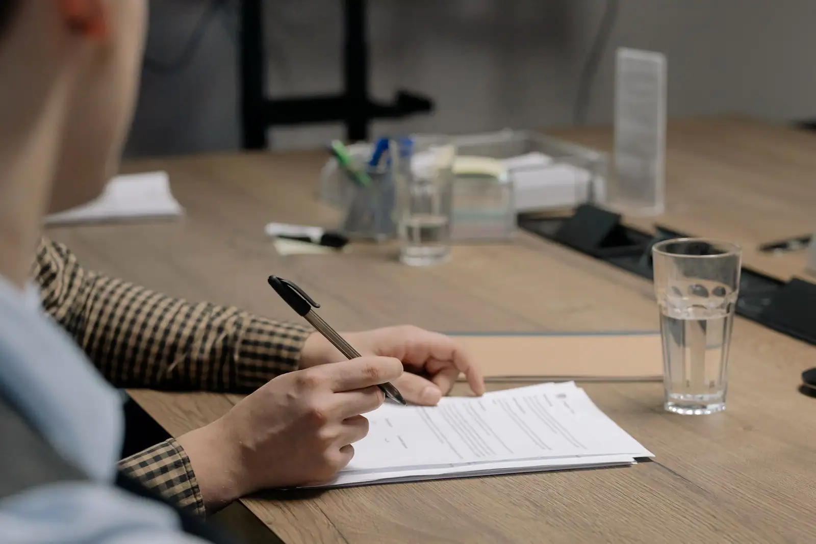 Une personne signe un document sur la table d'un bureau, stylo en main et dossier ouvert.
