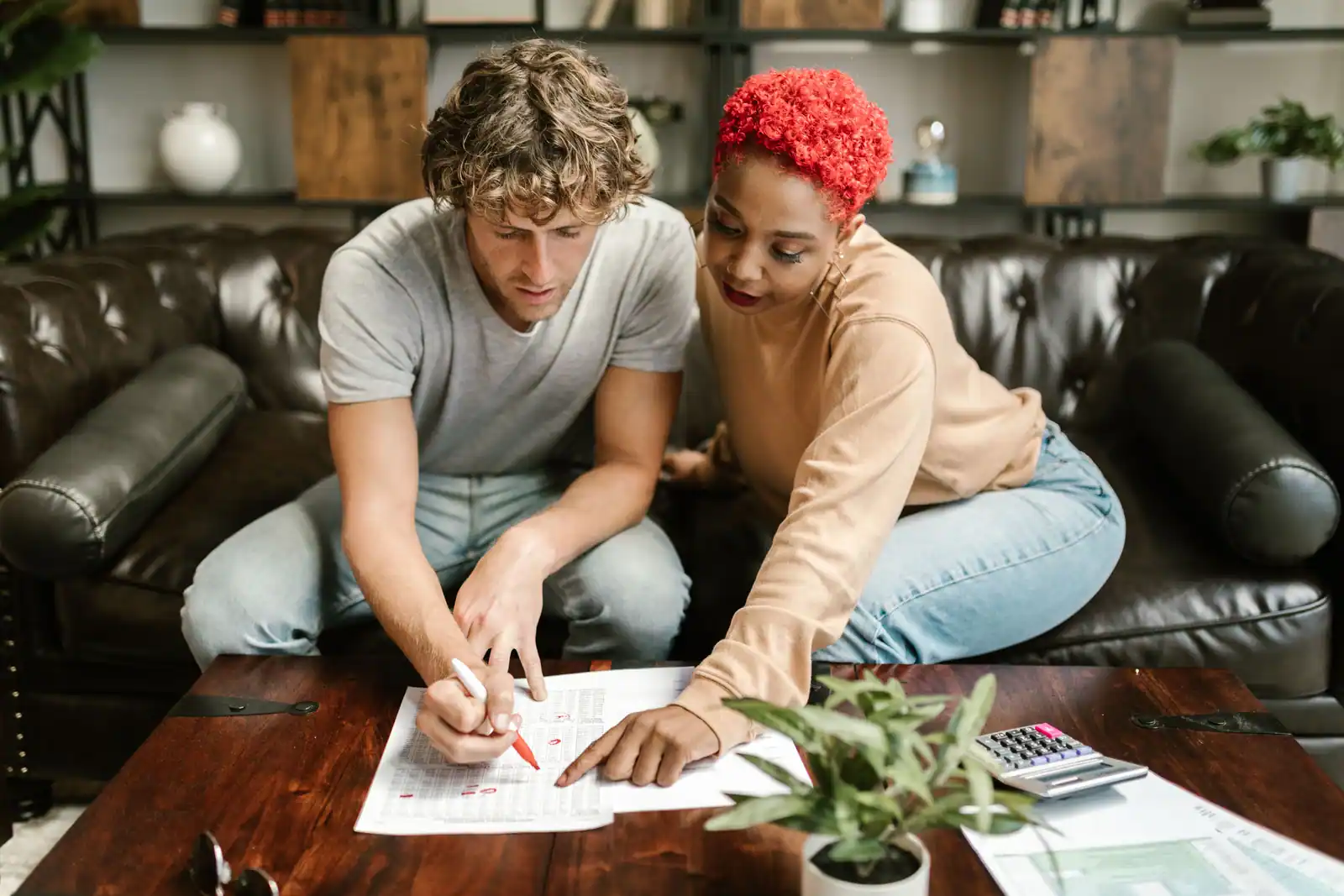 Deux personnes penchées sur un formulaire imprimé posé sur une table basse, l'une annotant au stylo rouge.