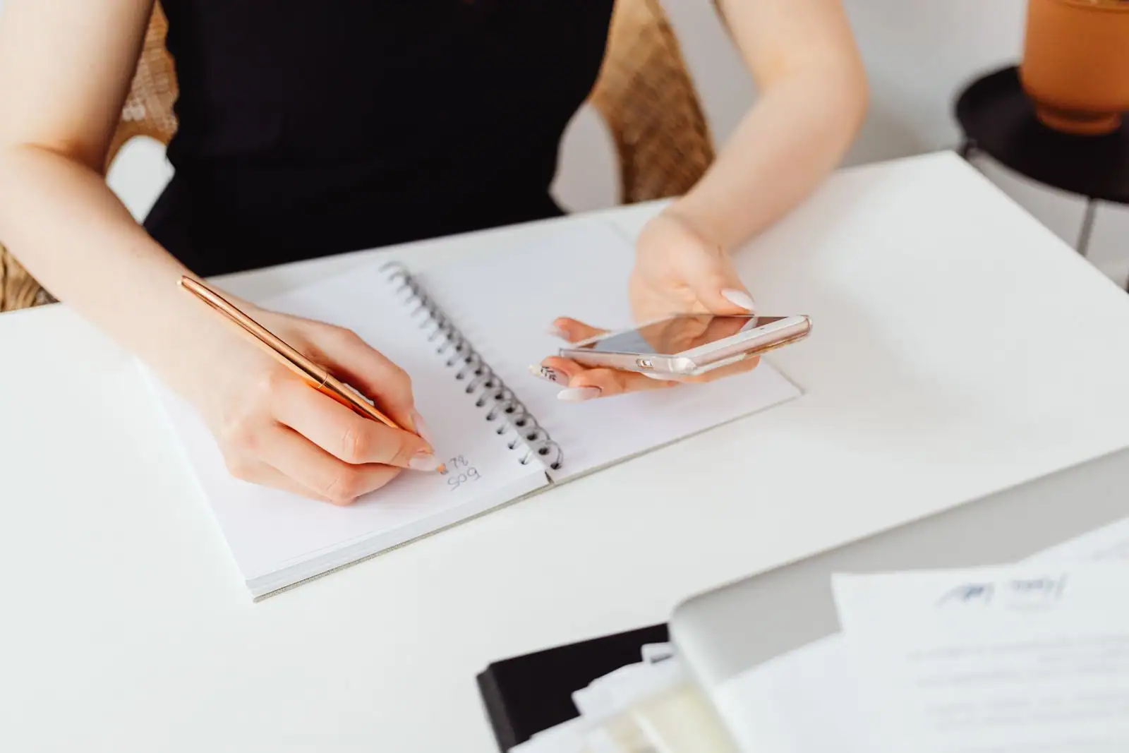 Une personne prend des notes sur un carnet à spirale tout en tenant son téléphone à la main.