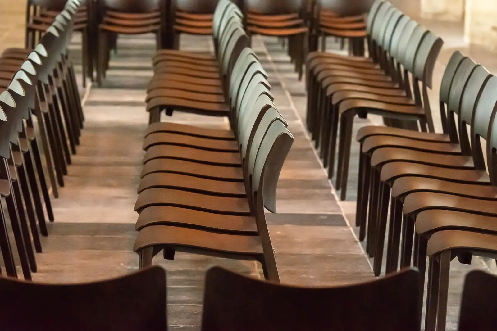Rangées de chaises en bois identiques alignées dans une salle, avant une assemblée générale