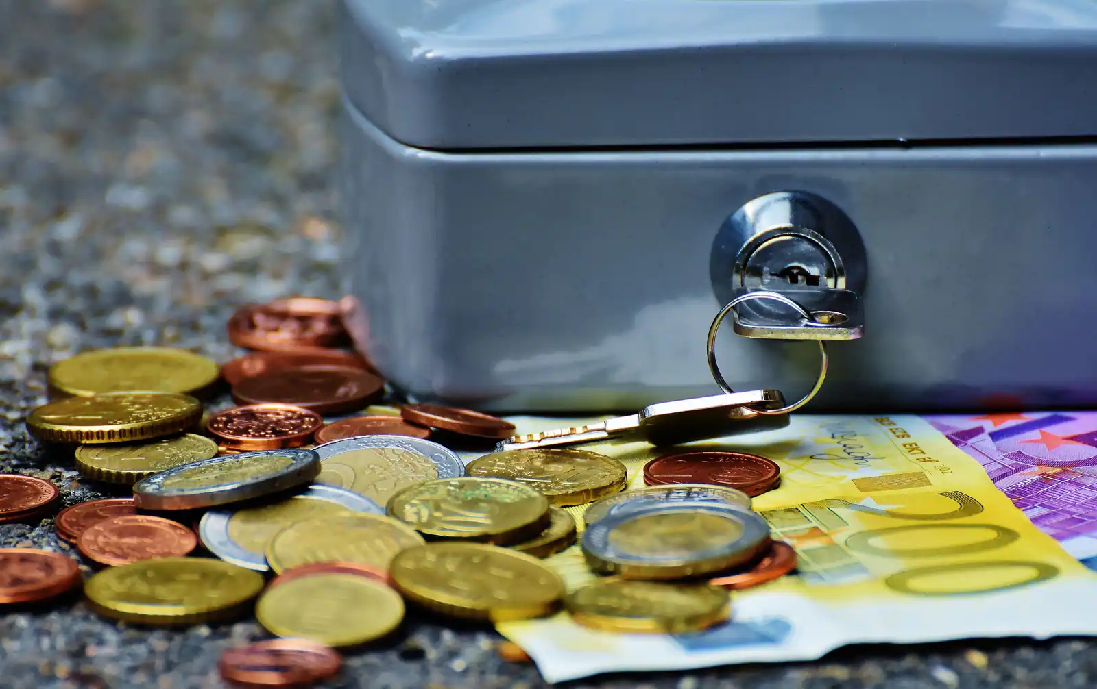 Caisse métallique avec sa clé sur la serrure, entourée de pièces et de billets en euros