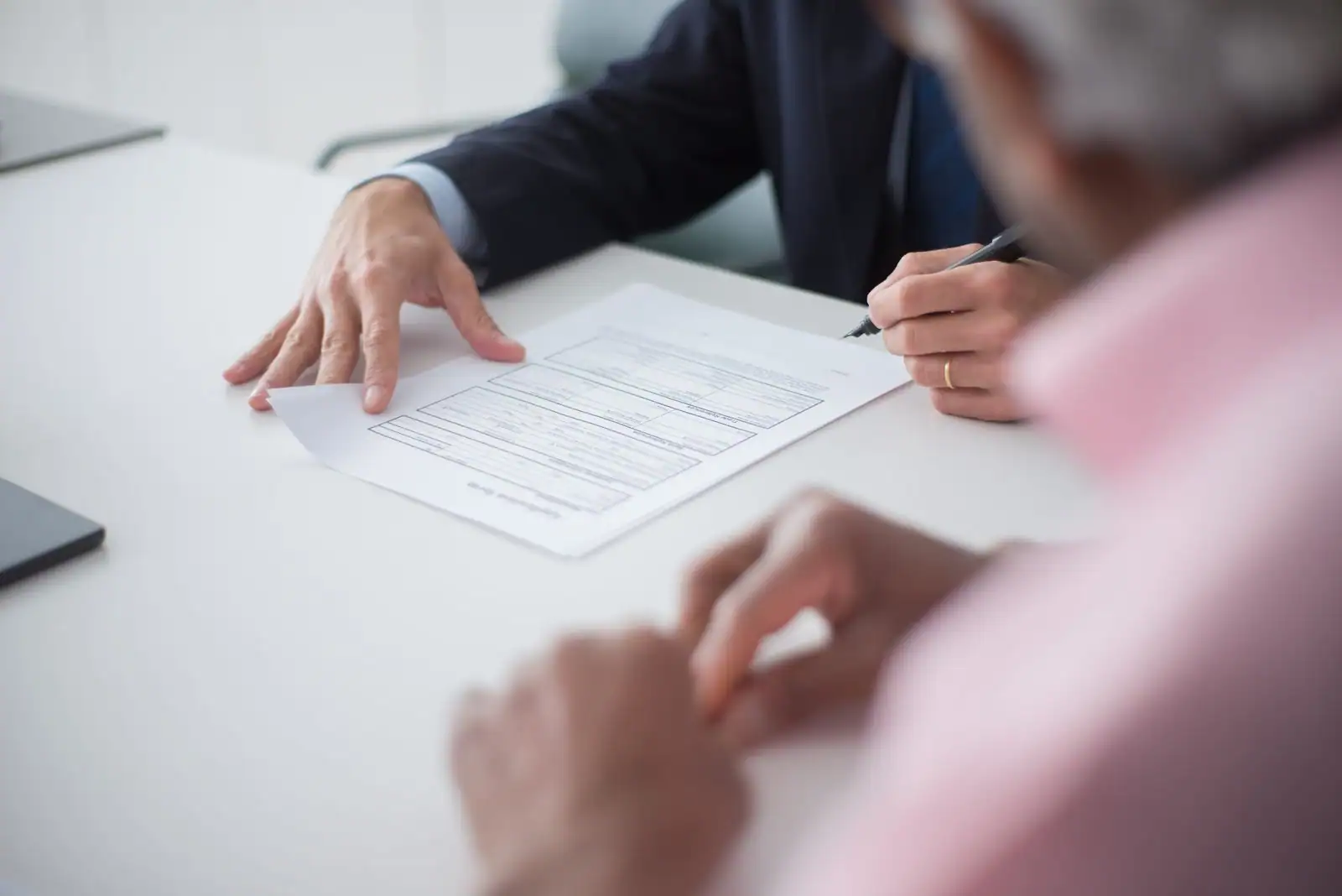 Un client signe un document sur une table de bureau, en présence d'un conseiller en costume.