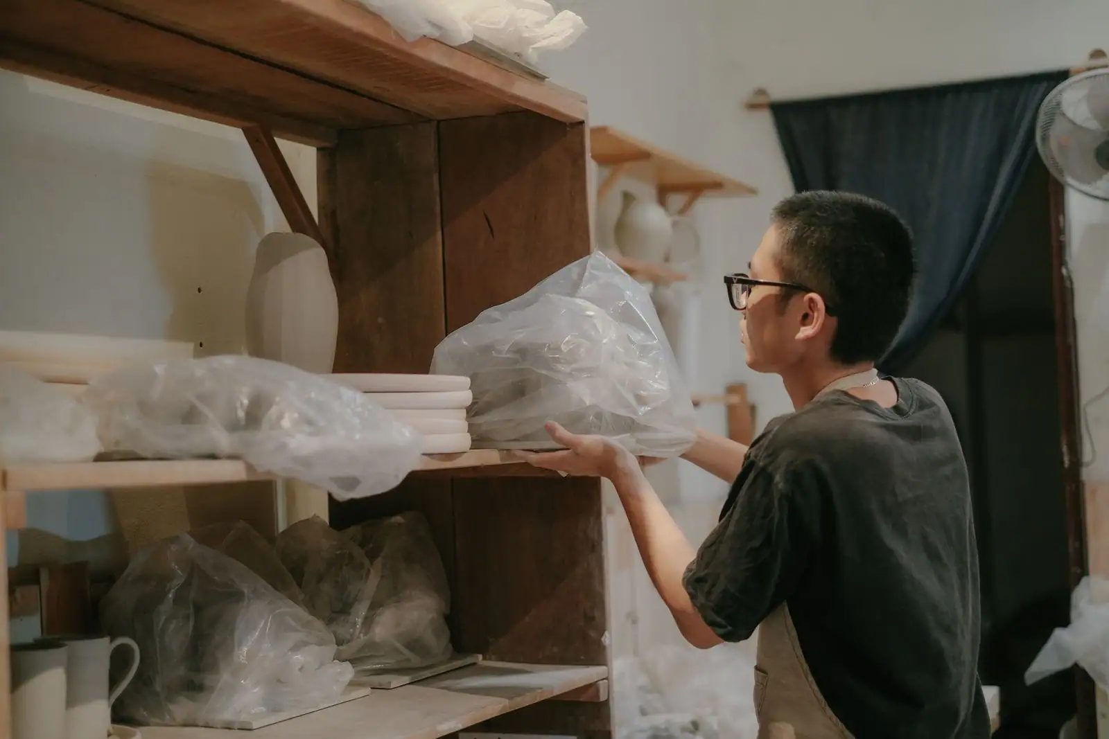 Un artisan céramiste range des pièces et de la terre sur les étagères de son atelier indépendant.