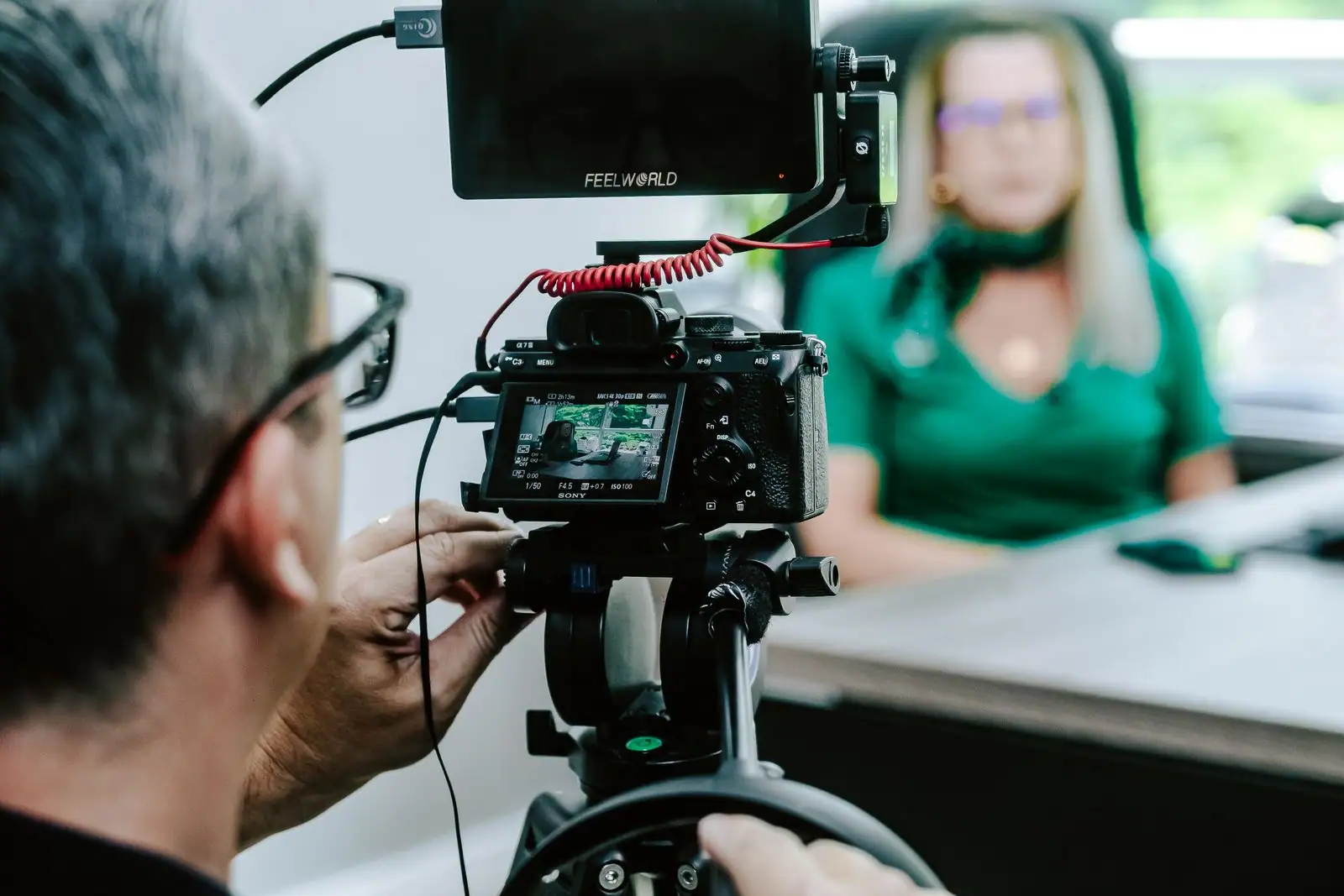 Un cadreur filme une salariée assise à son bureau pour un témoignage vidéo destiné à l'entreprise.