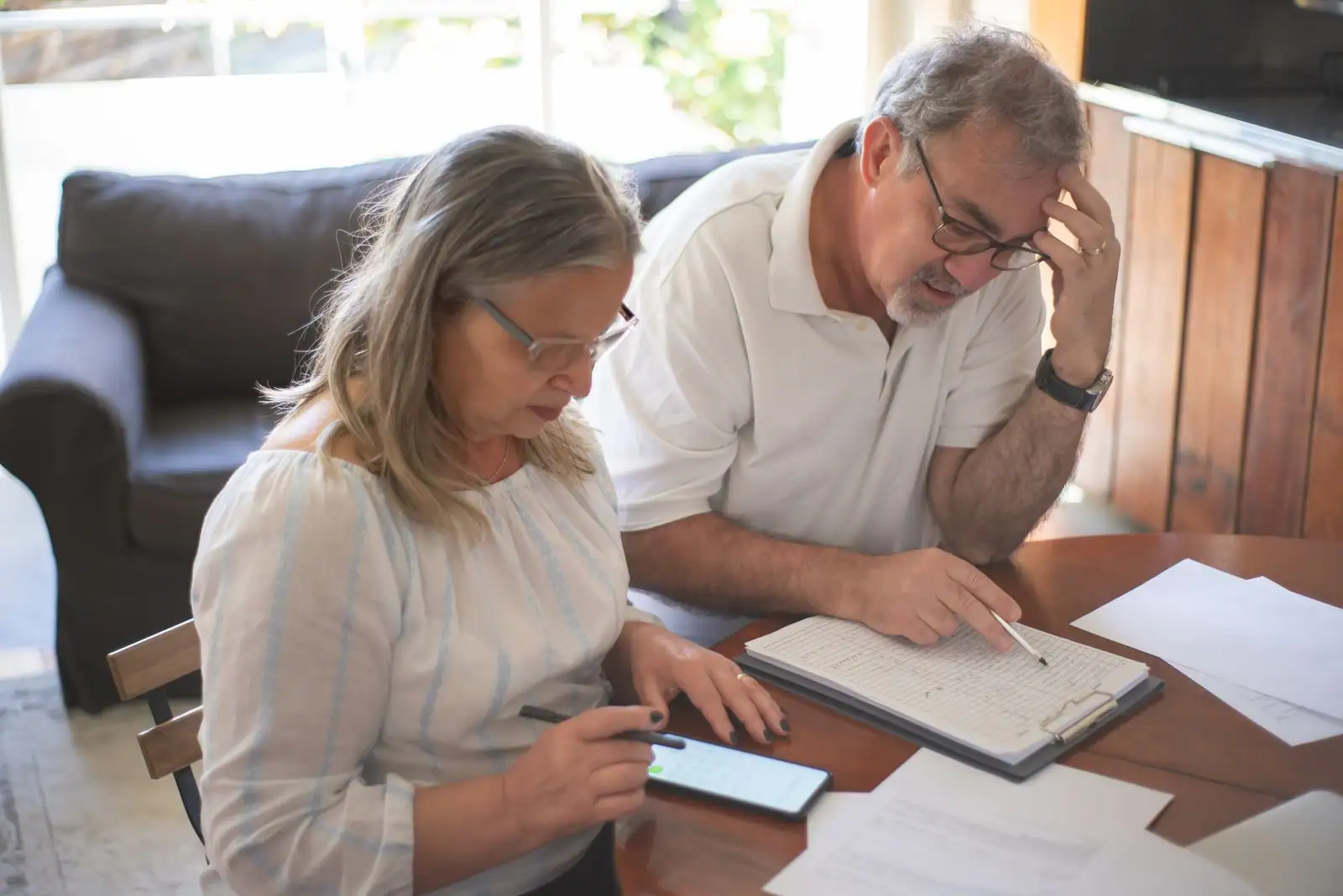 Couple attablé devant des documents papier, un stylo à la main et un téléphone affichant une calculatrice
