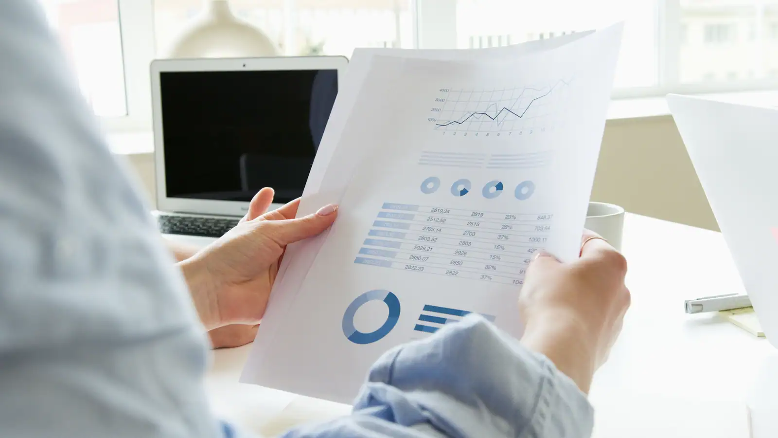 Une personne examine les pages imprimées d'un rapport financier, graphiques et tableaux chiffrés.