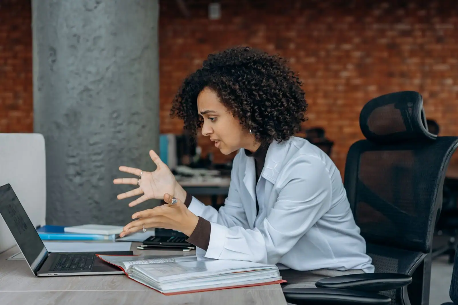 Une femme assise à un bureau lève la main dans un geste d'incompréhension face à son ordinateur portable.