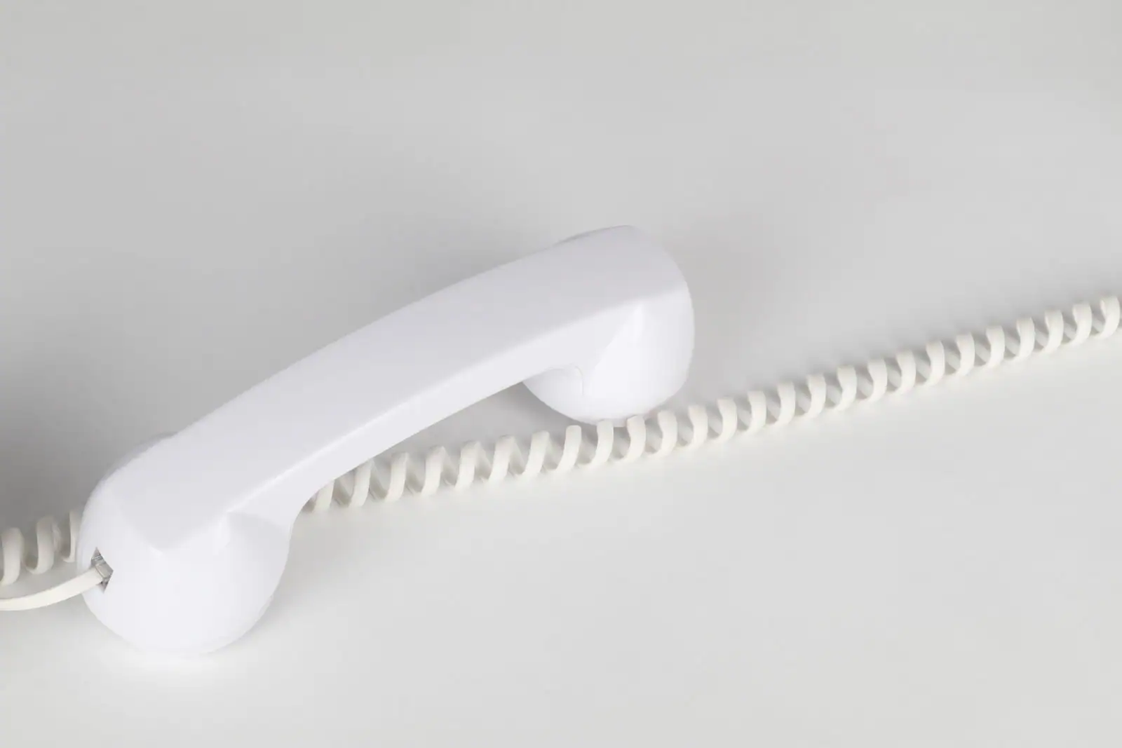 Combiné de téléphone filaire blanc posé hors de sa base, cordon spiralé déroulé sur fond clair