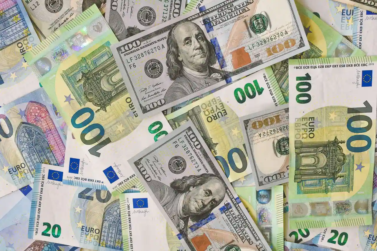 Des billets en euros et en dollars américains mêlés à plat, évoquant un compte multidevise.